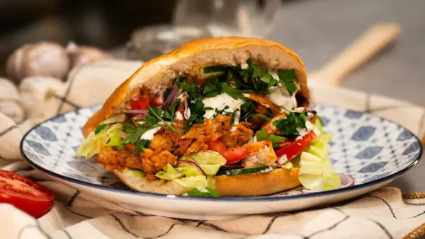 Pyszny, domowy kebab z kurczaka z piekarnika, pełen świeżych warzyw i sosu, na ozdobnym talerzu.