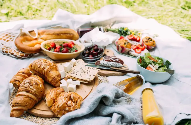 Pyszne jedzenie na piknik: świeże pieczywo, owoce, sałatka, sery i napoje.
